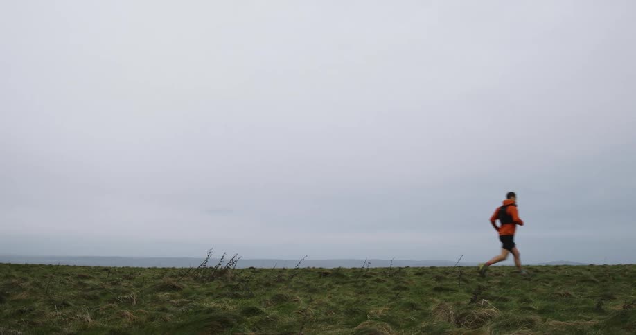 Person running in a grassy field on a cloudy day