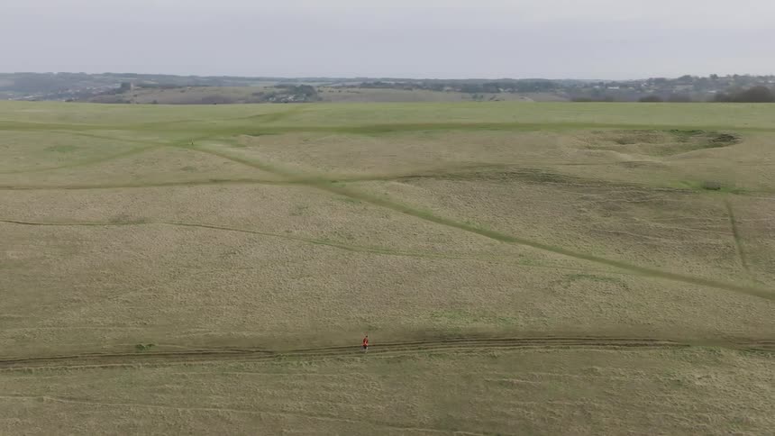 A person runs on a path across a vast grassy field in a rural area