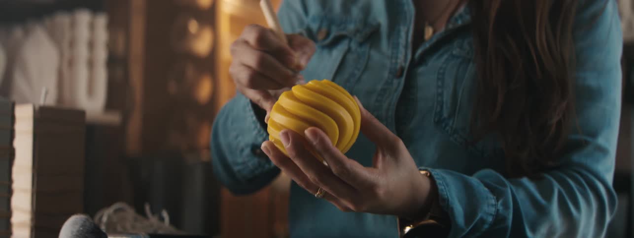 Hands of a female craftswoman working on a yellow spherical object