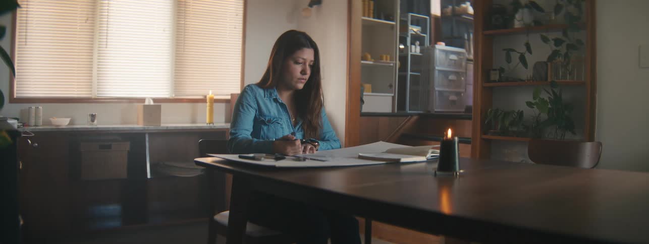 Woman sitting at the table writing and with a book in front of her