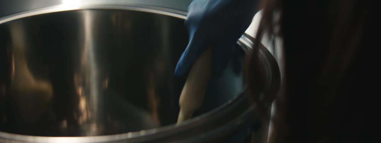 Gloved hand holding a spatula in a liquid in a pan