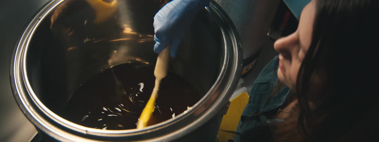 Woman wearing gloves and holding a spatula swirling a liquid inside a pan