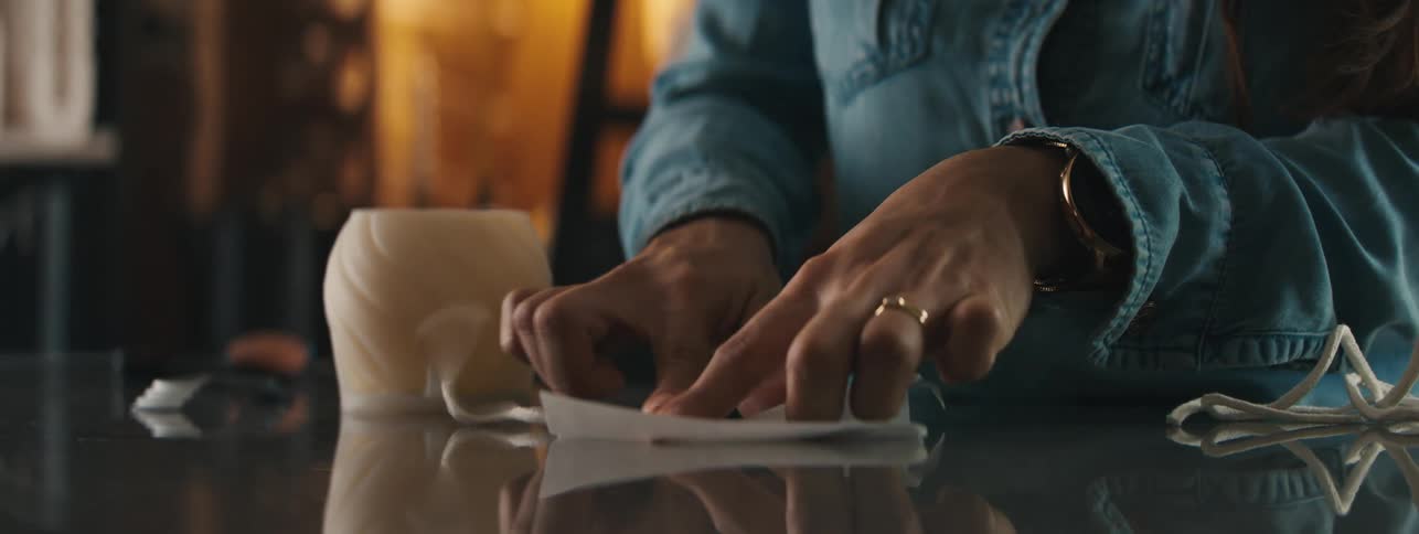 A woman wearing a blue denim shirt rubs her finger on a piece of paper in a garage