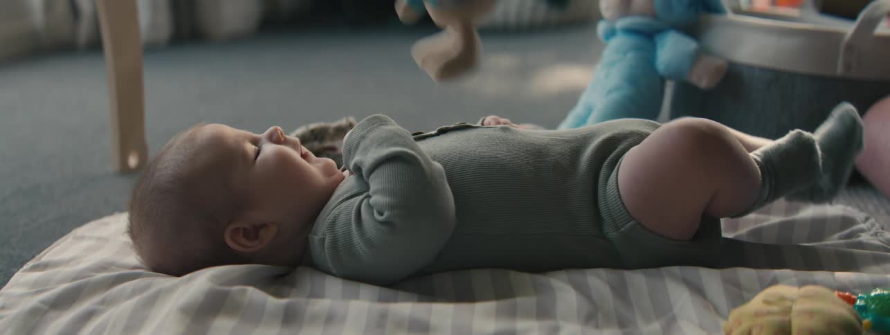 An adult using a toy rabbit to play with a baby thats lying on the floor in a blanket