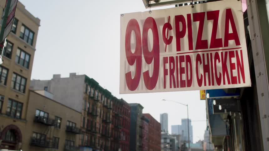 A sign for a fried chicken and pizza restaurant hangs outside a building in a city