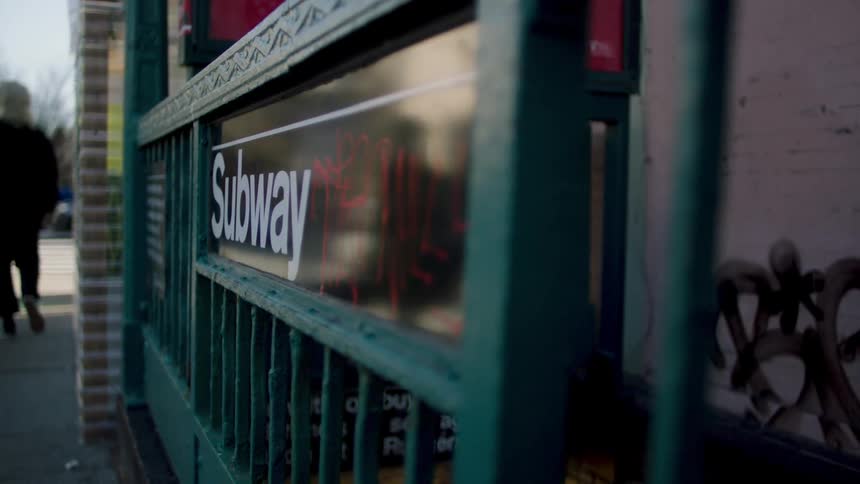 Pedestrians and cars move around a city near an entrance to the subway