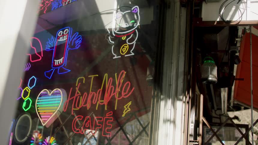Happy cat shaped neon sign waves in the window of a cafe
