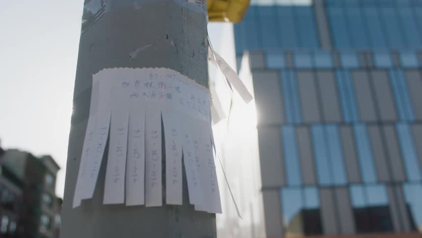 A piece of paper with writing on it and cut into partial strips taped onto a metal pole in a city
