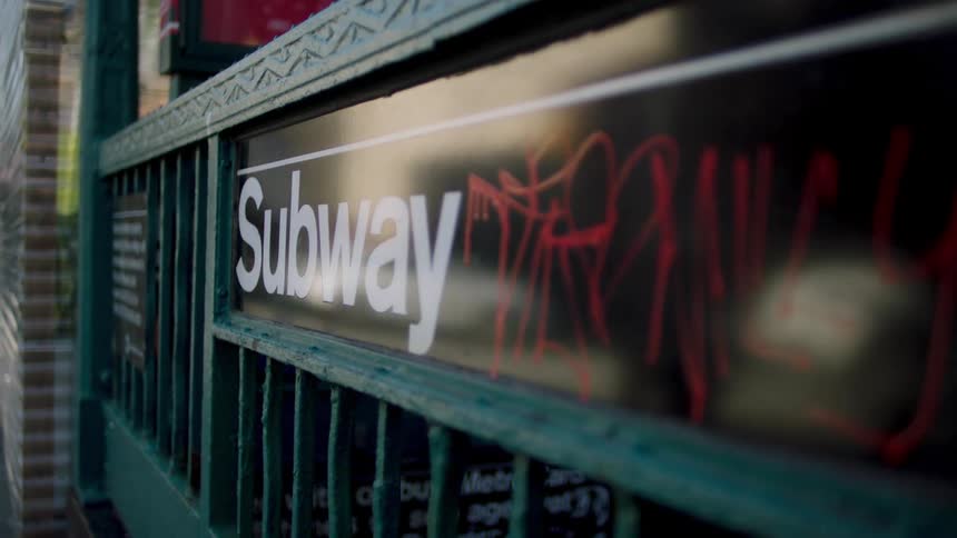 A close up of a subway sign with red graffiti