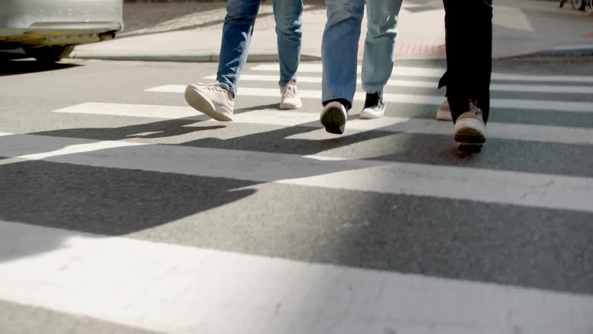 Three people crossing a road on a crosswalk walking synchronized and side by side