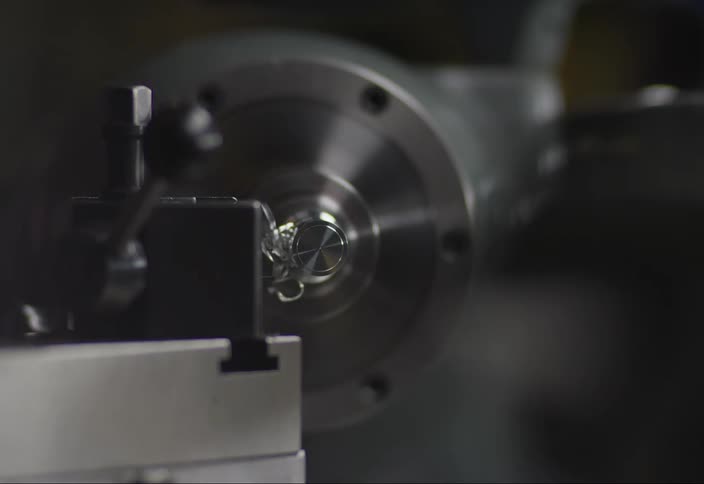A lathe scrapes off metal strands from metal which an employee pulls away and tosses