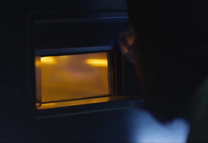 Person with glasses looking intently at a microwave