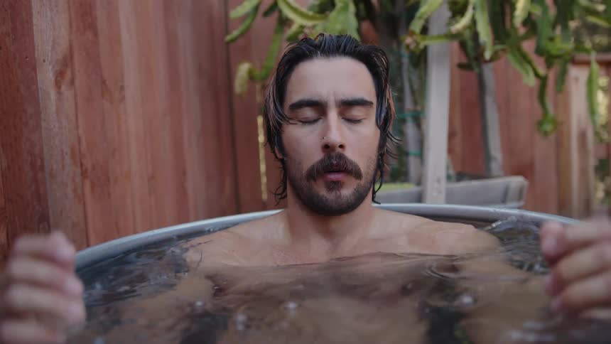 A man sits inside a small metal bath tub then closes his eyes