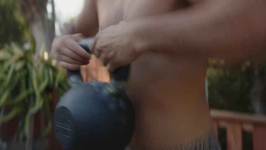 Shirtless man doing sumo squats holding a weight in his hands