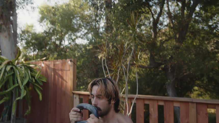A strong muscular man lifting a kettlebell outdoors in the backyard