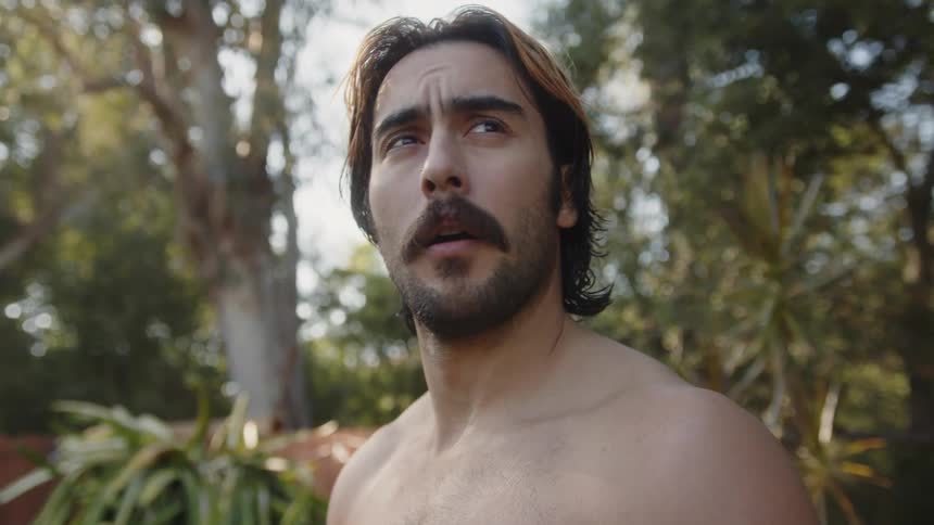 A man who looks slightly sad stretches his head and neck while standing in a yard