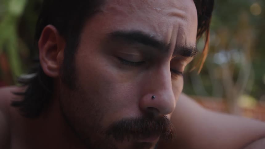 A shirtless contemplative man runs his fingers through his hair