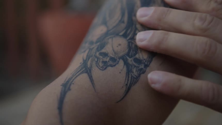 Person strokes their tattoo which incorporates skulls
