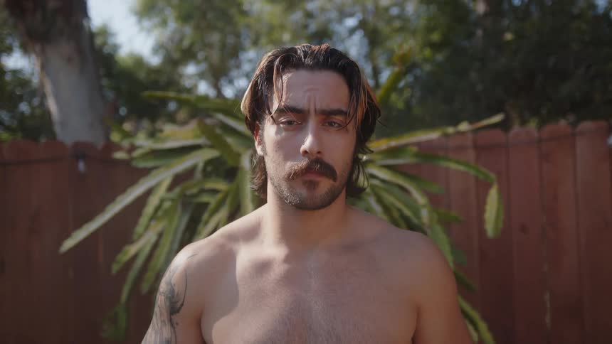 A man standing in a back yard tightens the laces on his shorts then runs his fingers through his hair
