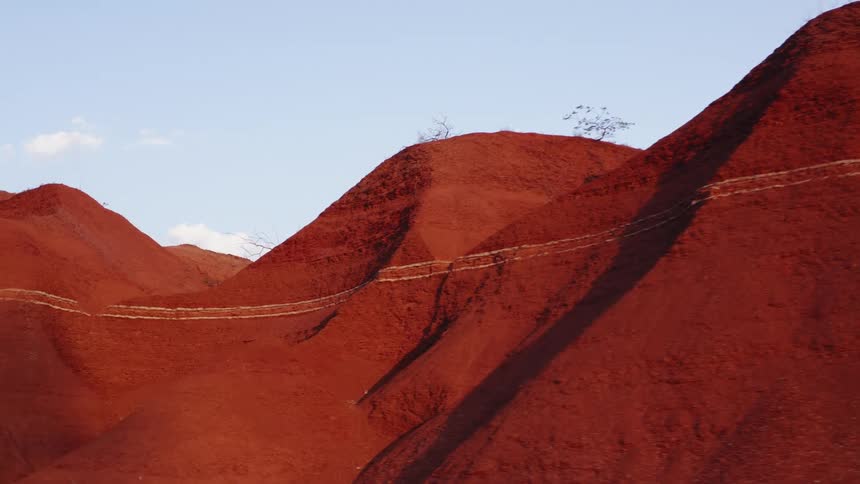 Series of red sand hills with distinct horizontal stratification lines under a clear blue sky