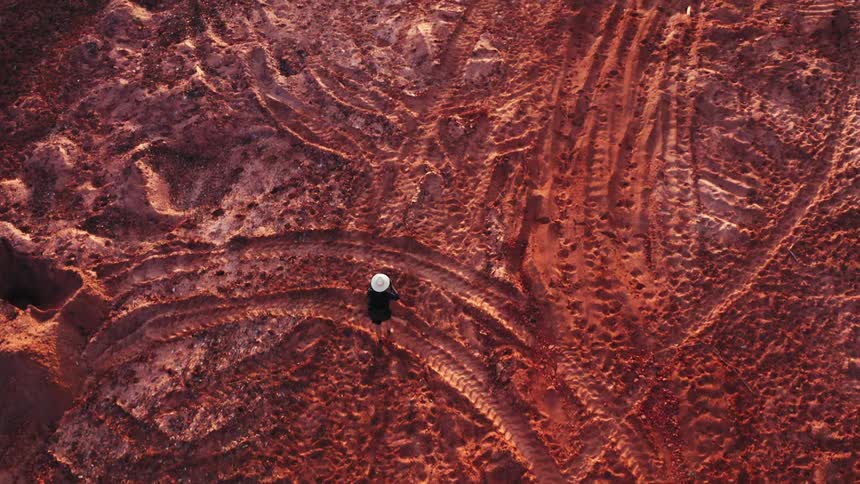 Someone walking over red sand terrain full of tire tracks