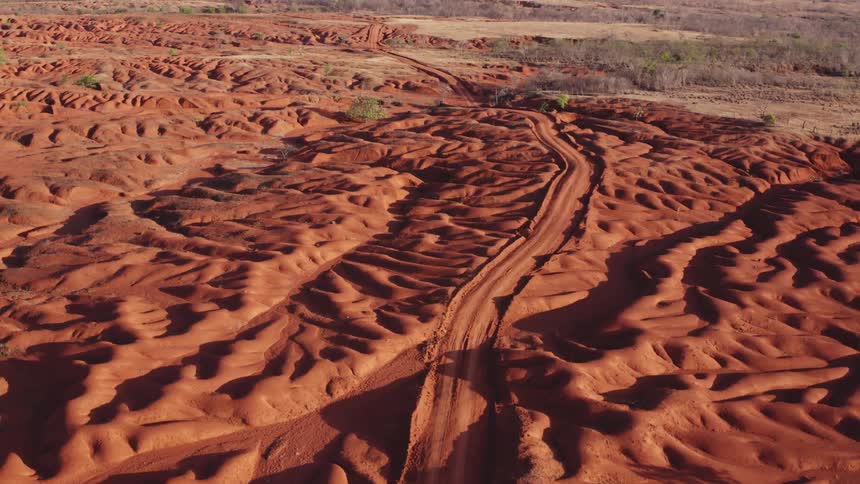 Dirt road passes through arid red hills while haze covers the plateaus in the distance
