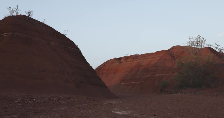 Mounds of red earth with distinct layers visible against a clear blue sky