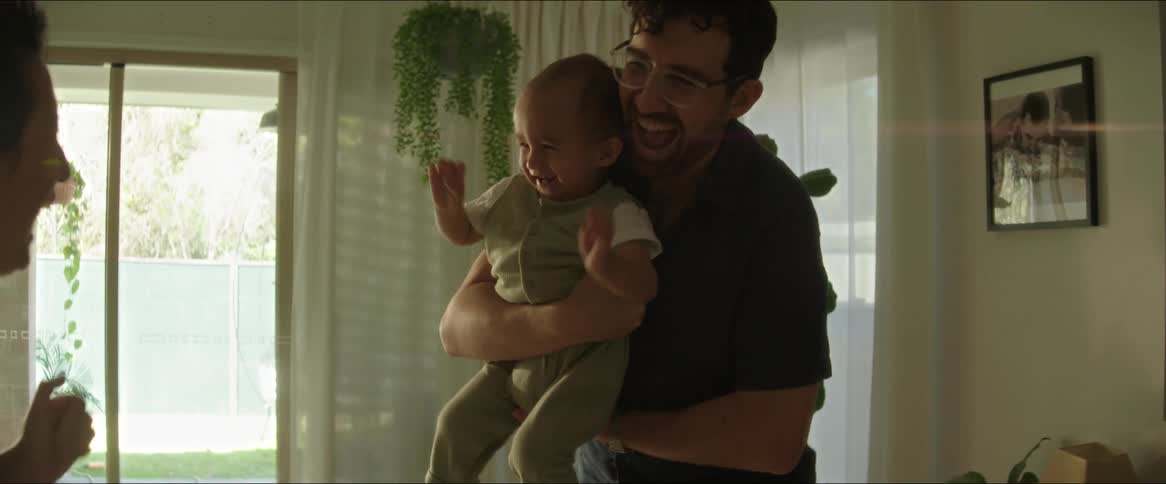 A grandmother and a father holding a baby laugh as they walk around a living room