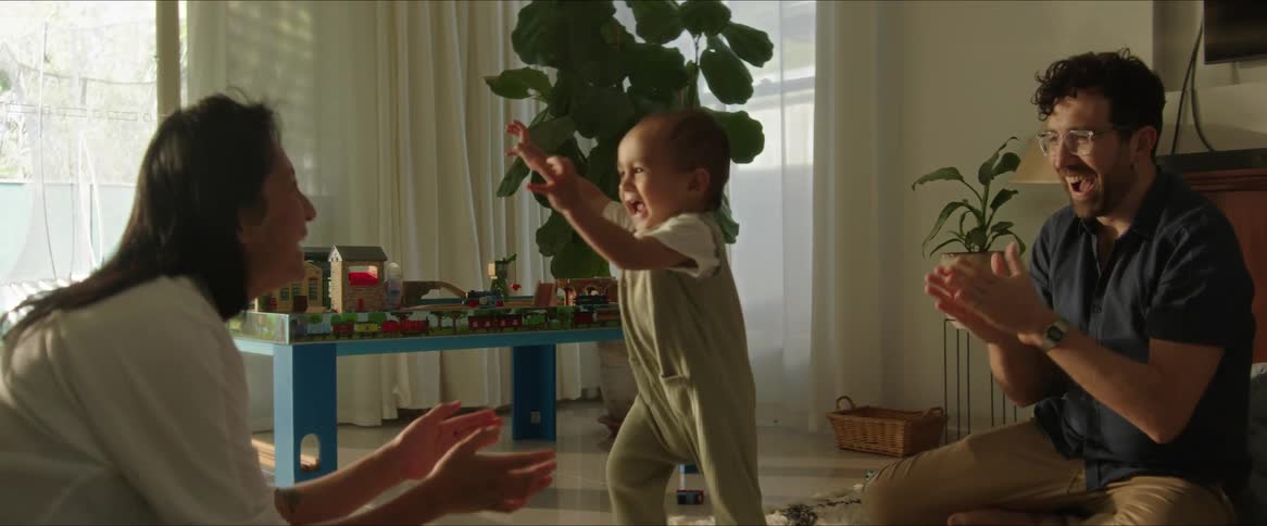 A toddler walks from his father to his mother across a living room rug