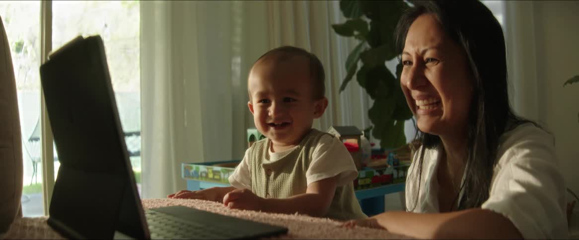 A mother and her toddler son look at a laptop and laugh together