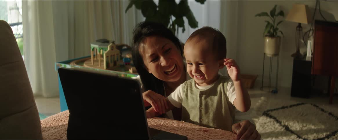 Smiling mother and child wave during a video call made from their living room