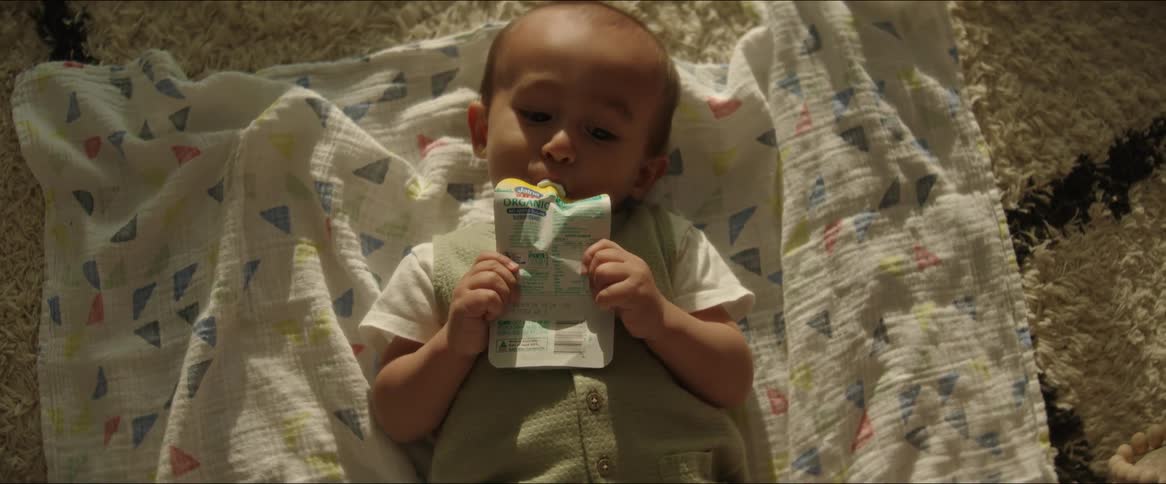 A baby is laying on the ground drinking a juice pouch