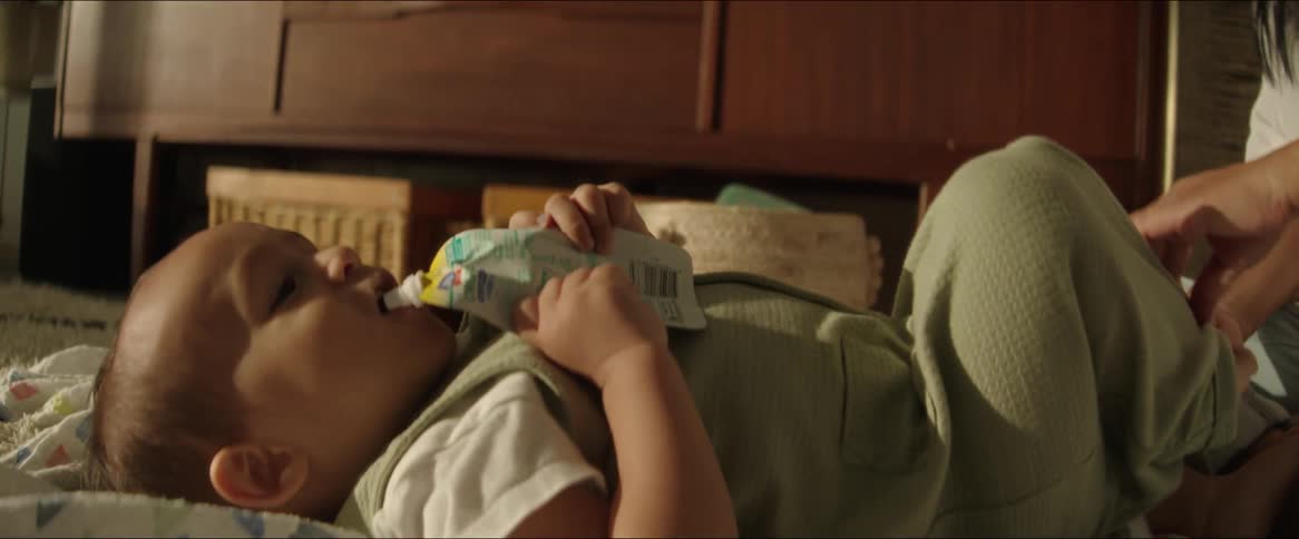A mother watches her baby drink from a juice pouch