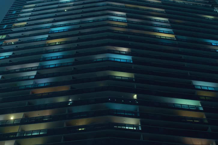 A tall residential building seen at night with the colorful lights turning on together