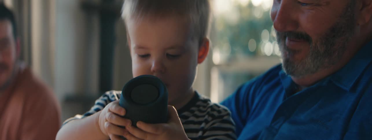 Toddler interacting with a bluetooth speaker with his father and grandfather together