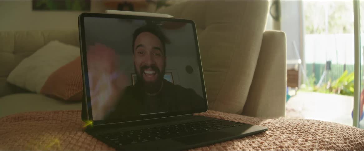 A tablet computer displays a video call with a smiling man waving