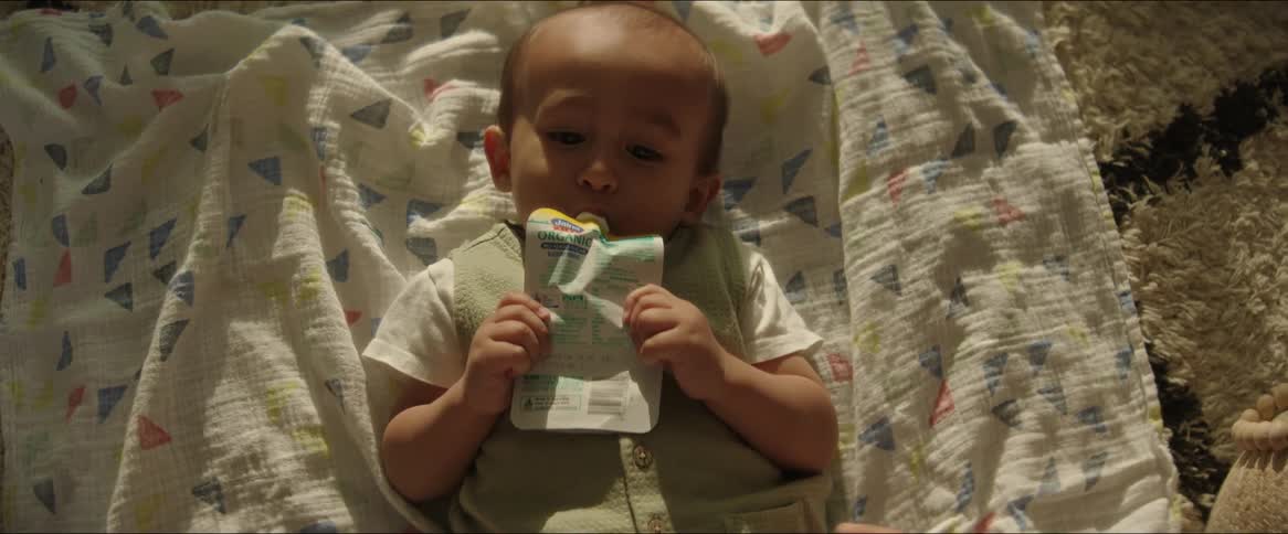 A baby is laying on a blanket drinking a juice pouch