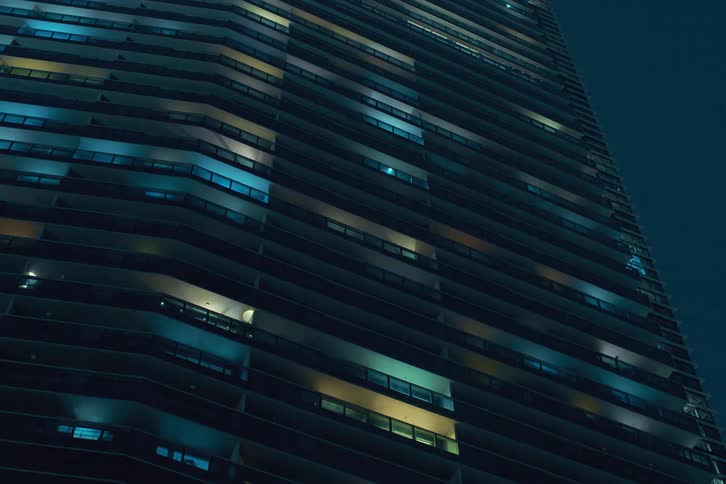 A clip of a building with many floors as it’s colorful window lights turn on together
