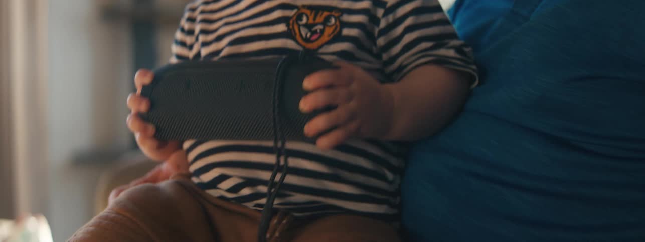 Small child sitting on fathers lap holding a bluetooth speaker