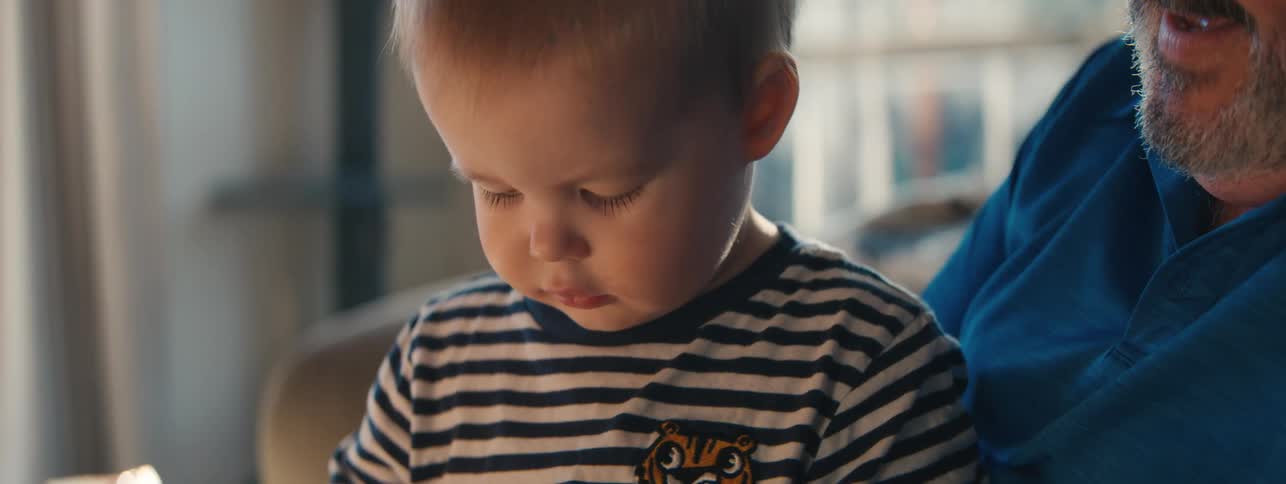 An older man talks to a toddler who is grabbing an electronic device