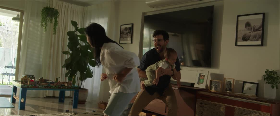 Father chases his wife while carrying their infant child in the living room