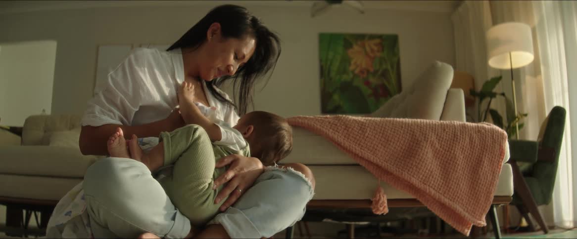 A woman is crouching on the floor breastfeeding her baby who is on her lap and she is happy