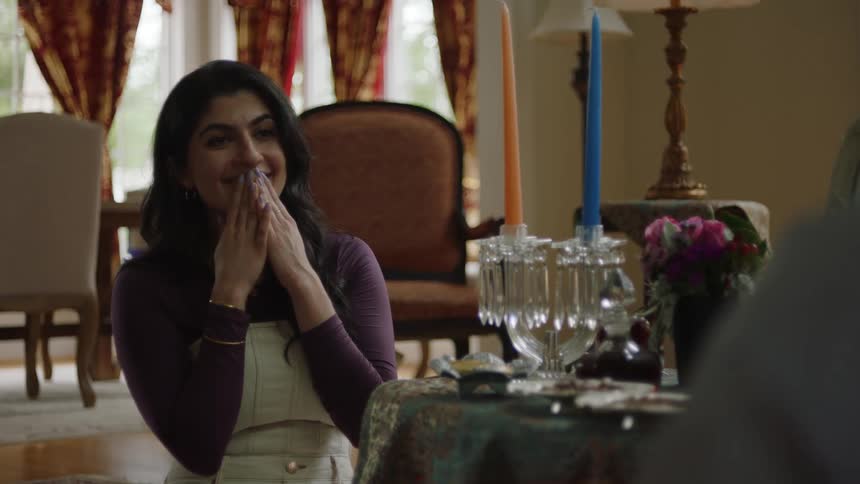 An indian woman holds her hands to her mouth while she smiles during a discussion with another woman sitting at a table