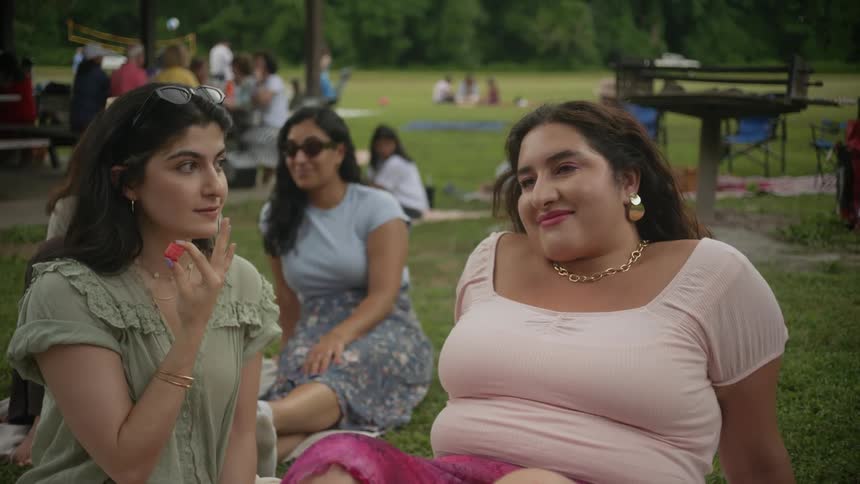 Two friends sitting on the grass with people around watching