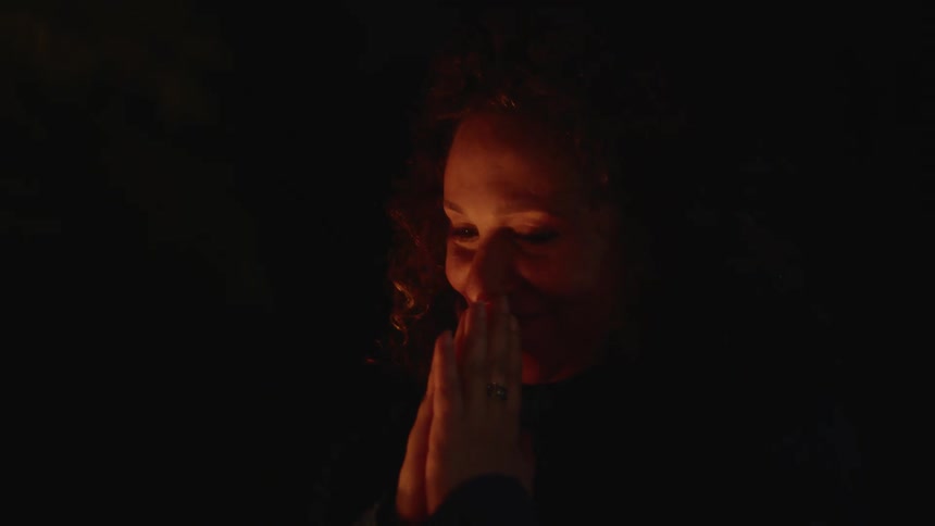 Woman in a dark environment with a happy facial expression clapping her hands