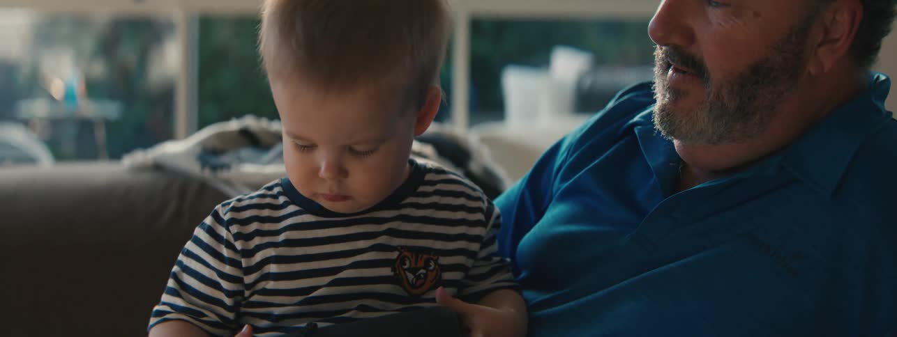 A man holds a toddler and laughs as the child examines an object