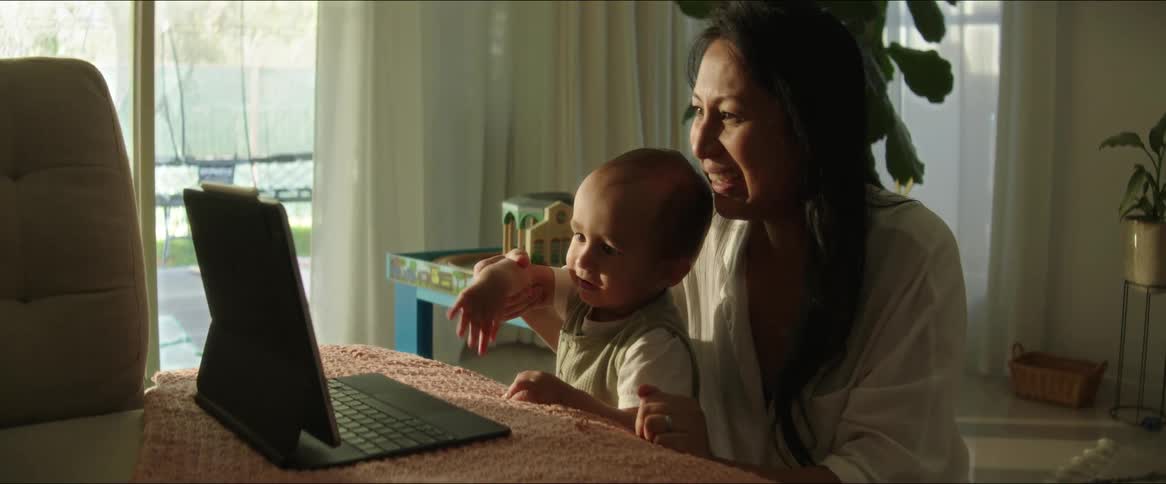 Mother helps her child wave during a video call at home
