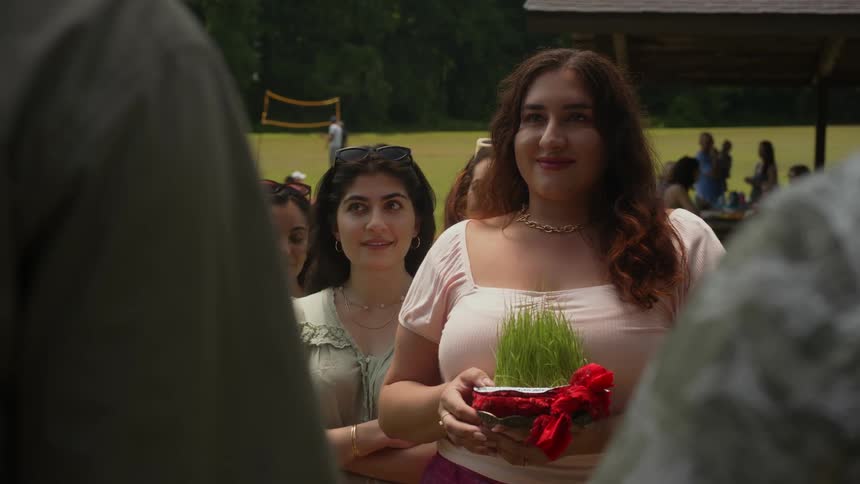 Woman in a field surrounded by people smiling and holding a gift of green leaves