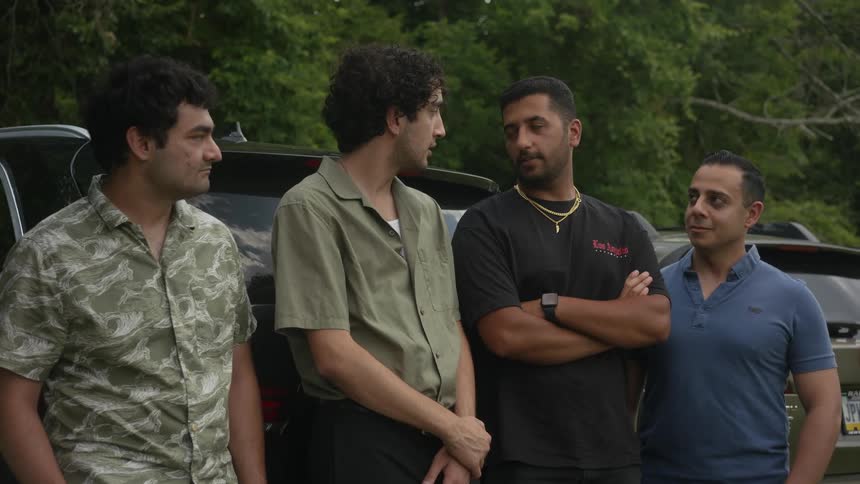 Four men stand in front of a car and carry on a discussion