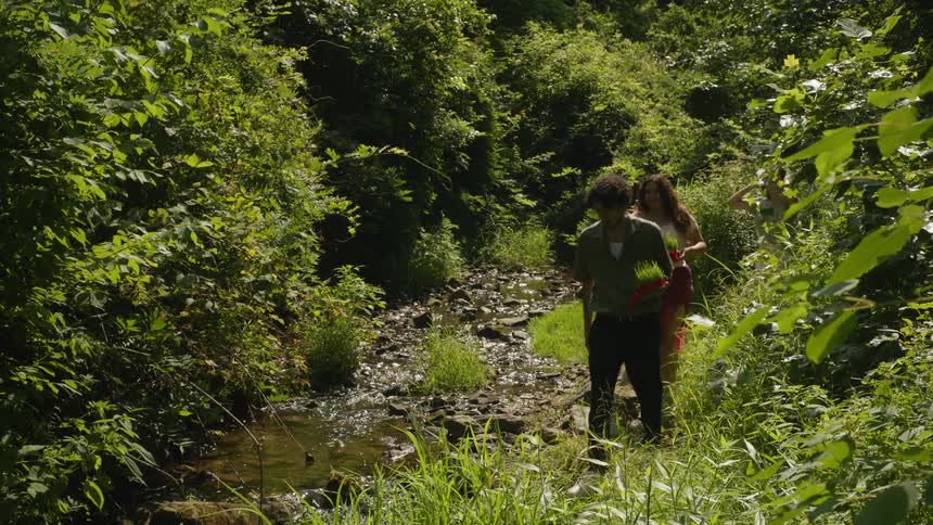 Group of young friends with flowers in their hands walking along the bank of a river